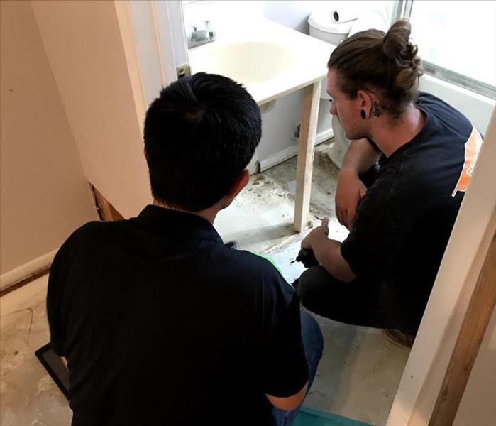 Two SERVPRO technicians prop a sink basin up with a wooden support beam