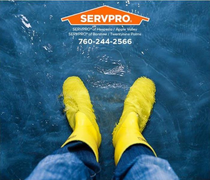 A person stands on a flooded floor in rubber boots.
