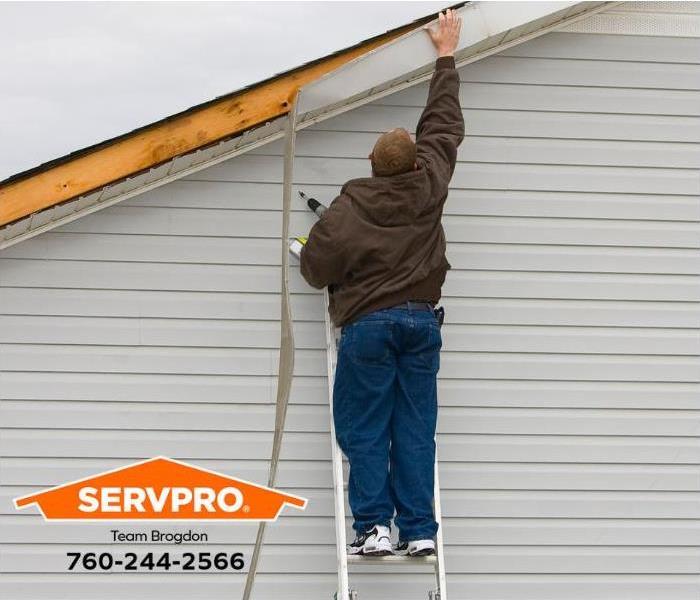 A homeowner repairs wind damage to the roof siding. 